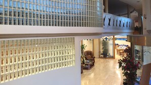 Eine Hotelhalle mit hoher Decke, einer Sitzecke mit braunem Ledersessel und einem dekorativen Glaseinsatz.