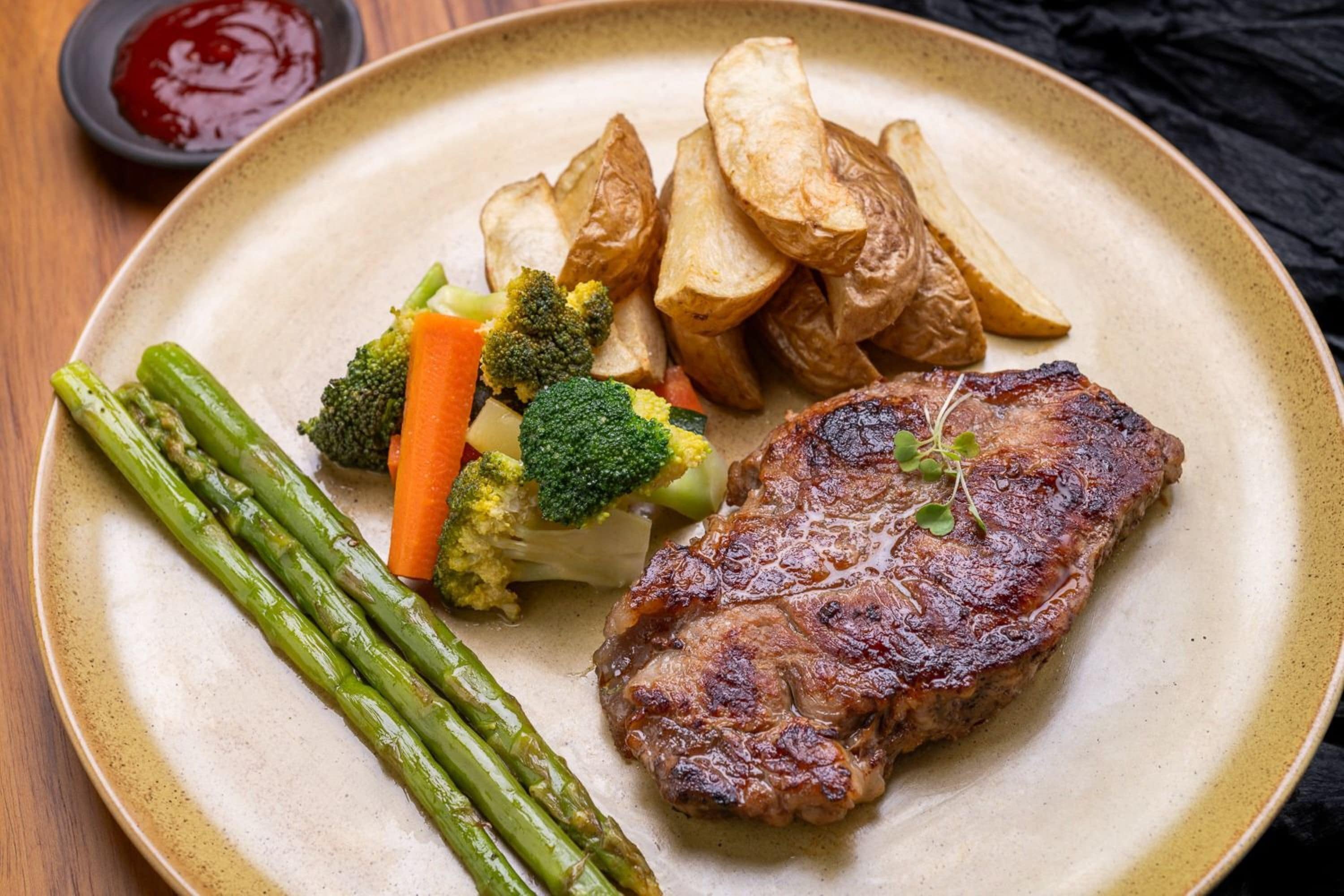 A plate with a steak, roasted potatoes, and steamed vegetables including asparagus and broccoli.