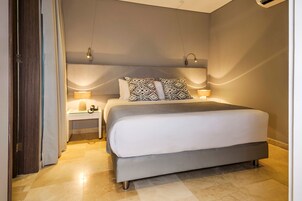 A modern bedroom with a large bed, two bedside tables with lamps, and a door to the left.