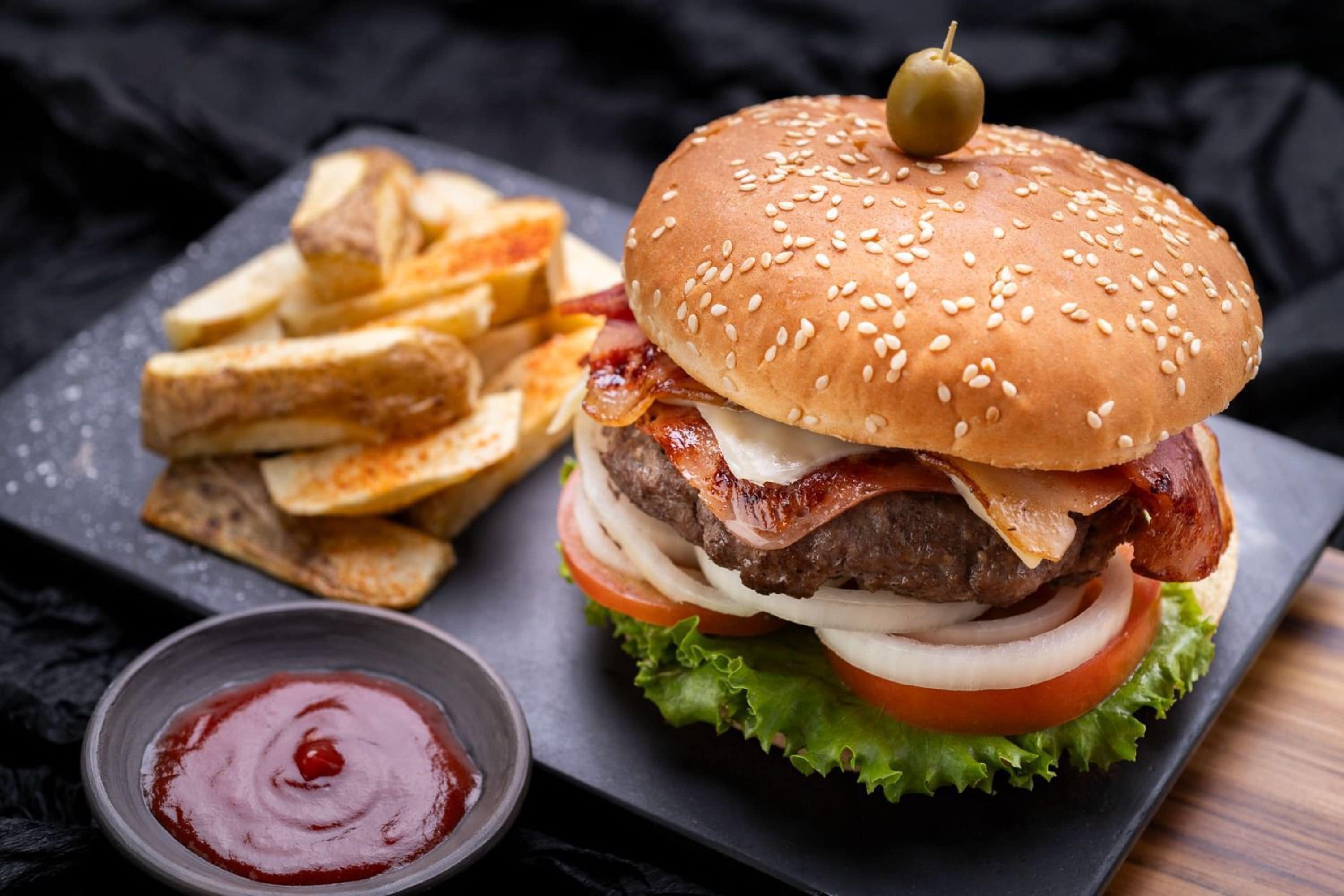 A burger with bacon, lettuce, tomato, and onion, served with fries and ketchup.