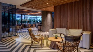 A modern interior with a wooden ceiling, a central seating area with wicker chairs, and a glass wall offering a view of the outdoors. - Hotel OZ Grand (Cartagena)