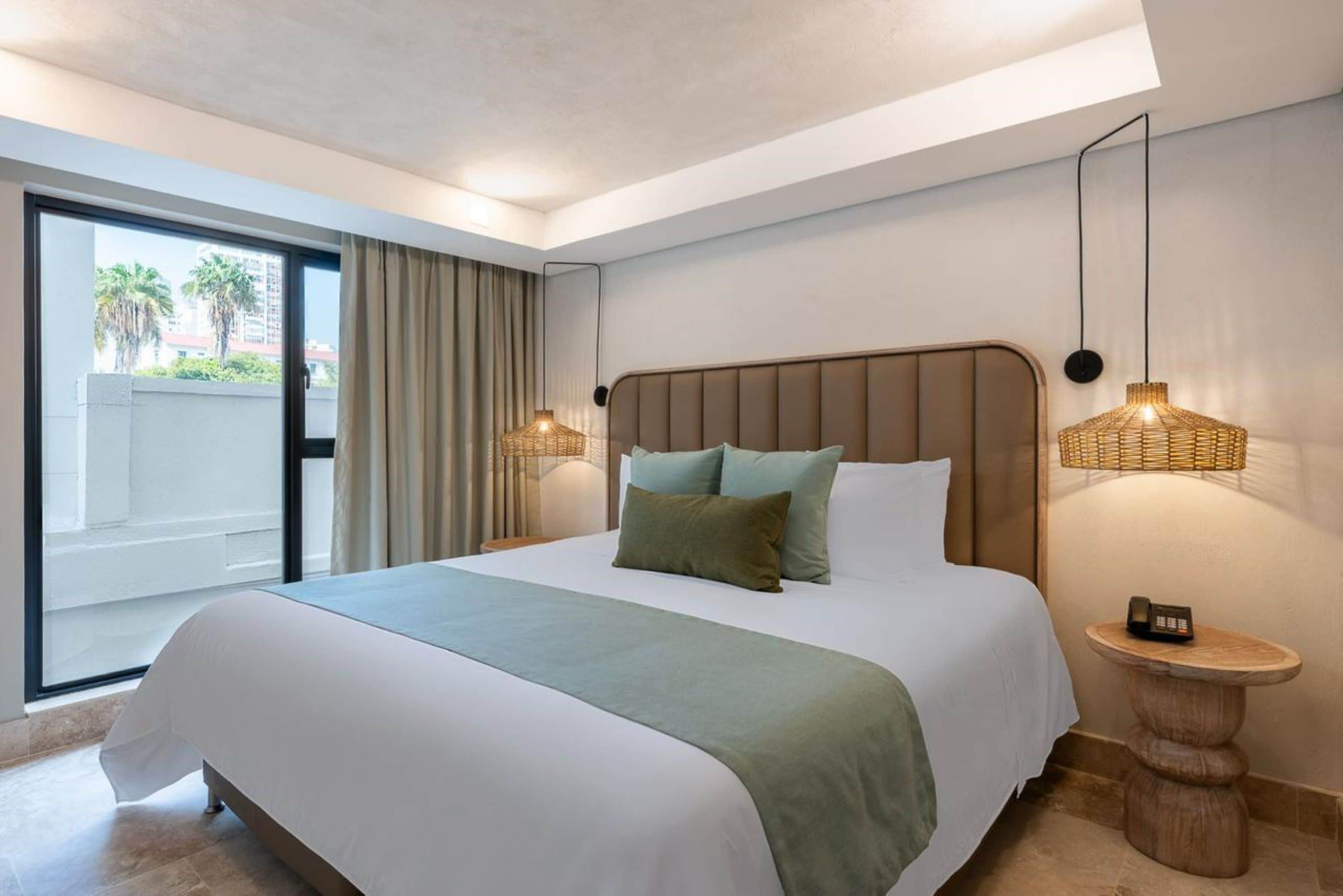 A modern hotel room with a large bed, a view of palm trees, and a balcony.
