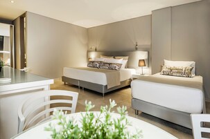 A modern hotel room with a large bed, a smaller bed, a desk, and a dining area.