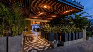 A modern hotel entrance with a wooden slatted roof, a geometric patterned walkway, and tropical plants. - Hotel OZ Grand (Cartagena)