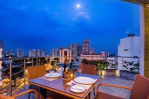 Un área de comedor en la azotea con vistas al horizonte urbano, mesas dispuestas para comer y plantas en macetas.