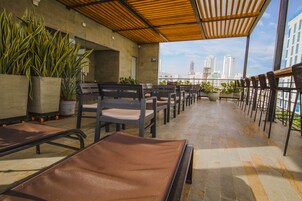 Una terraza en la azotea con asientos, plantas en macetas y vista al horizonte de la ciudad.