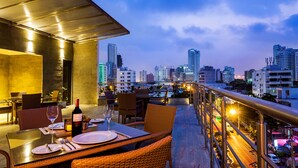 An outdoor dining area with tables and chairs, a city skyline in the background, and a view of the city. - Hotel OZ Grand (Cartagena)