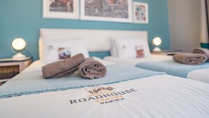 Hotelkamer met twee bedden, elk met een blauwe deken en een kussen met de naam van het hotel. Er hangen ingelijste foto's aan de muur en op elk nachtkastje staat een lamp.