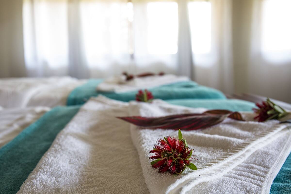 A bed with a white and teal towel, a red flower, and a leaf.
