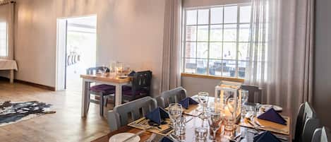 A dining area with a table set for four, a chandelier, and a view through the window.