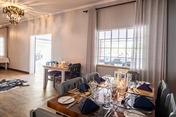 A dining area with a table set for four, a chandelier, and a view through the window.