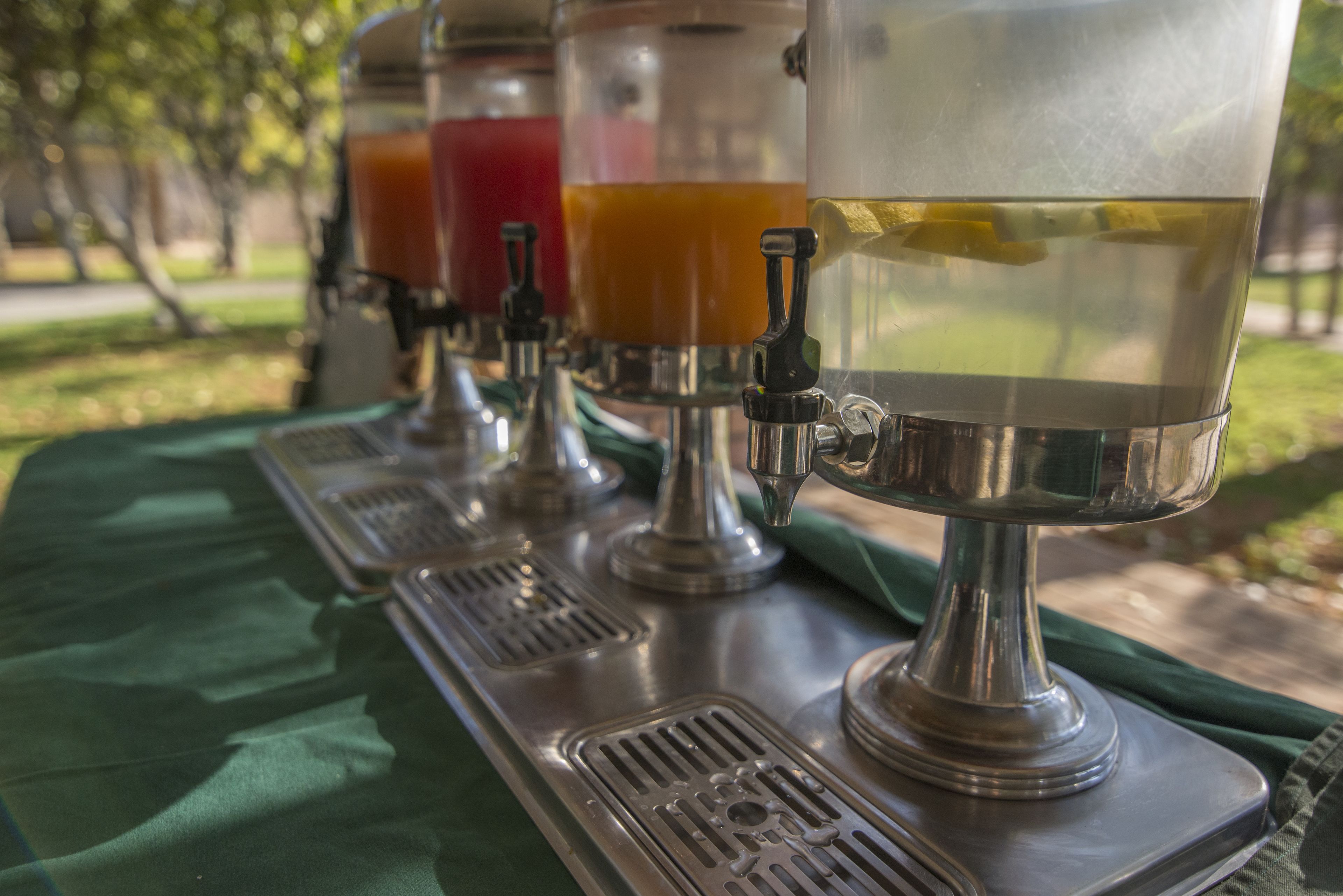 A row of beverage dispensers on a metal table outdoors.
