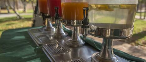 A row of beverage dispensers on a metal table outdoors.