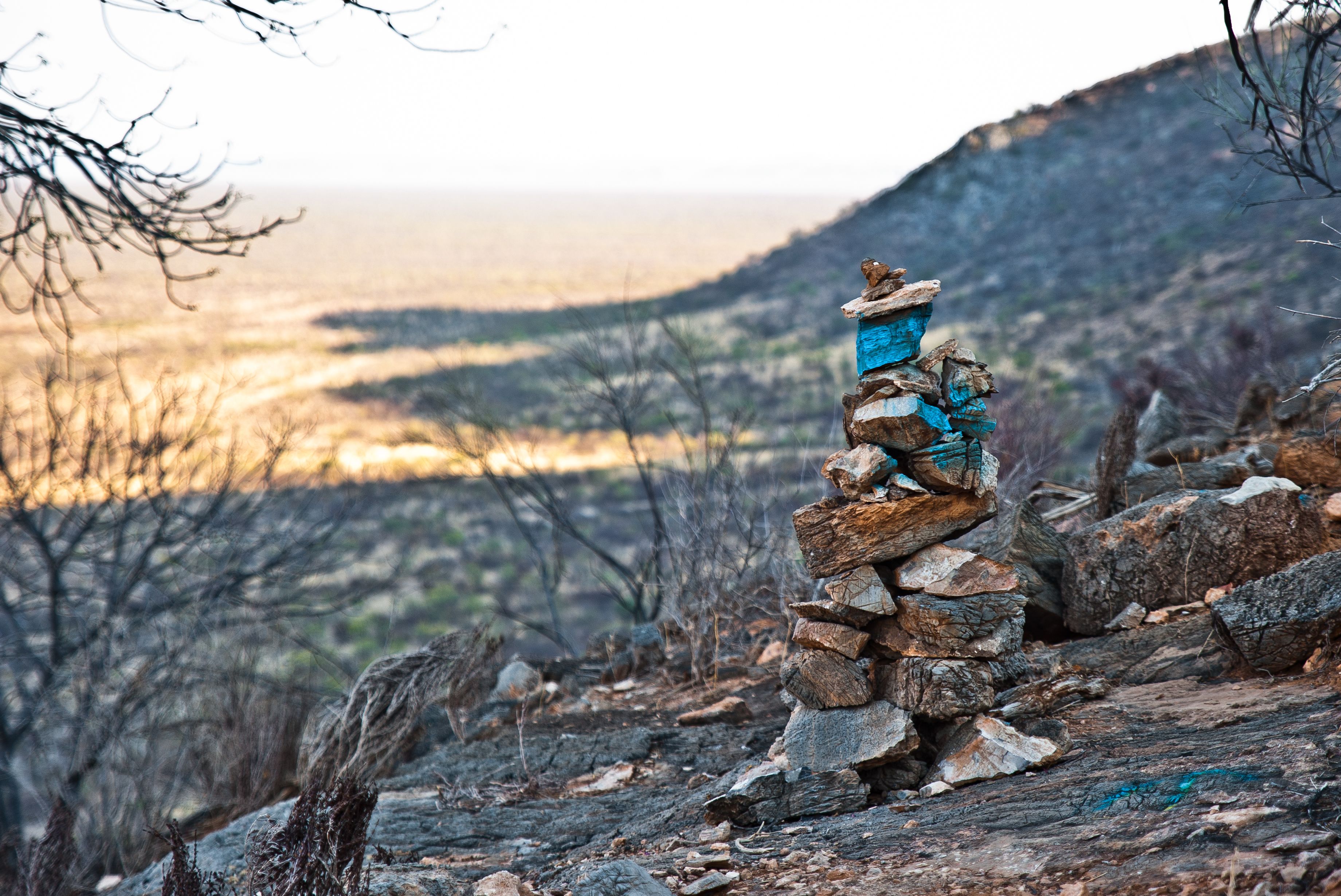 A stack of rocks with a blue object on top, set against a hilly landscape with sparse vegetation.