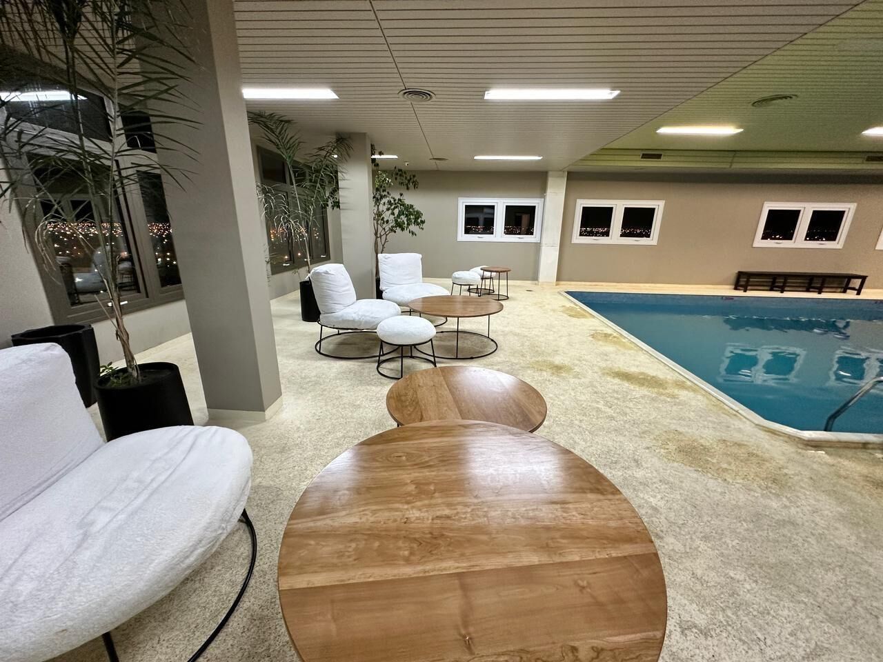 A pool area with a wooden table and chairs, a white sofa, and a view of the pool.