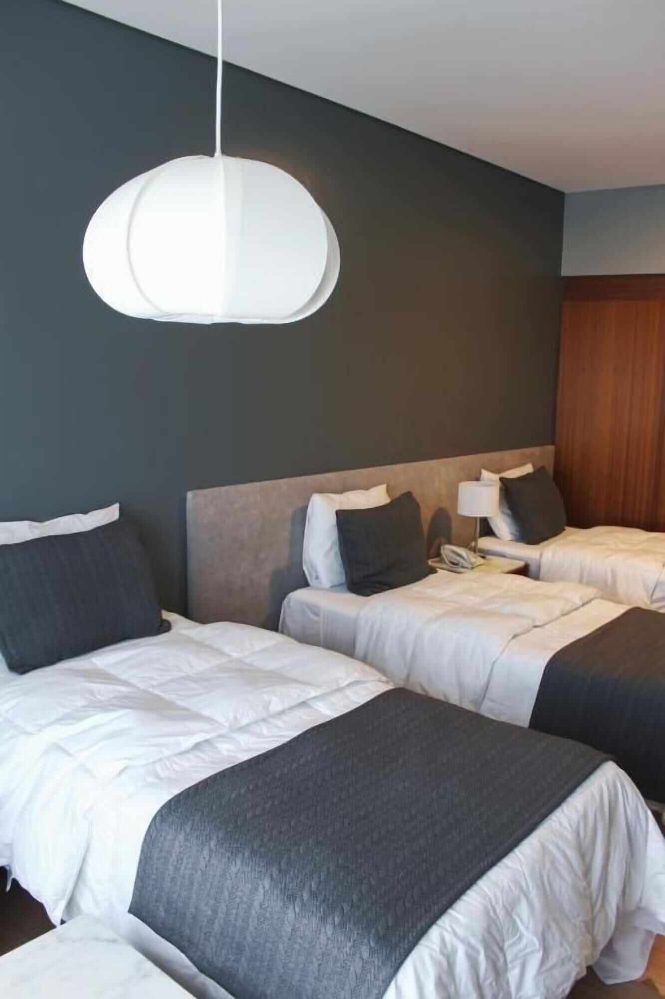 A hotel room with two beds, a modern pendant light, and a wooden wardrobe.