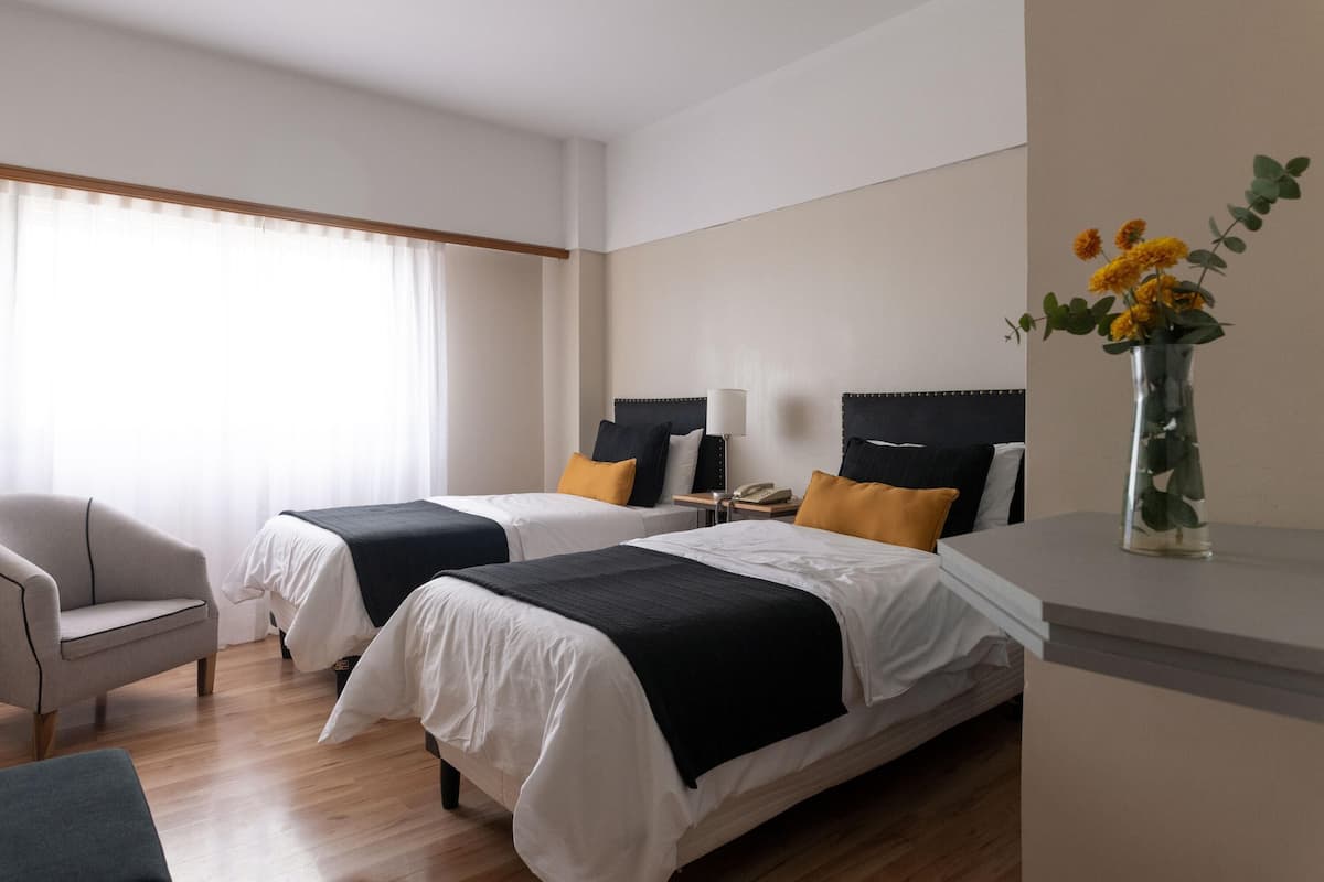 Une chambre d’hôtel avec deux lits, une chaise, une table de chevet et un vase avec des fleurs.