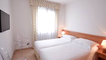 Habitación de hotel con dos camas, una silla, una mesita de noche con lámpara y un televisor montado en la pared.