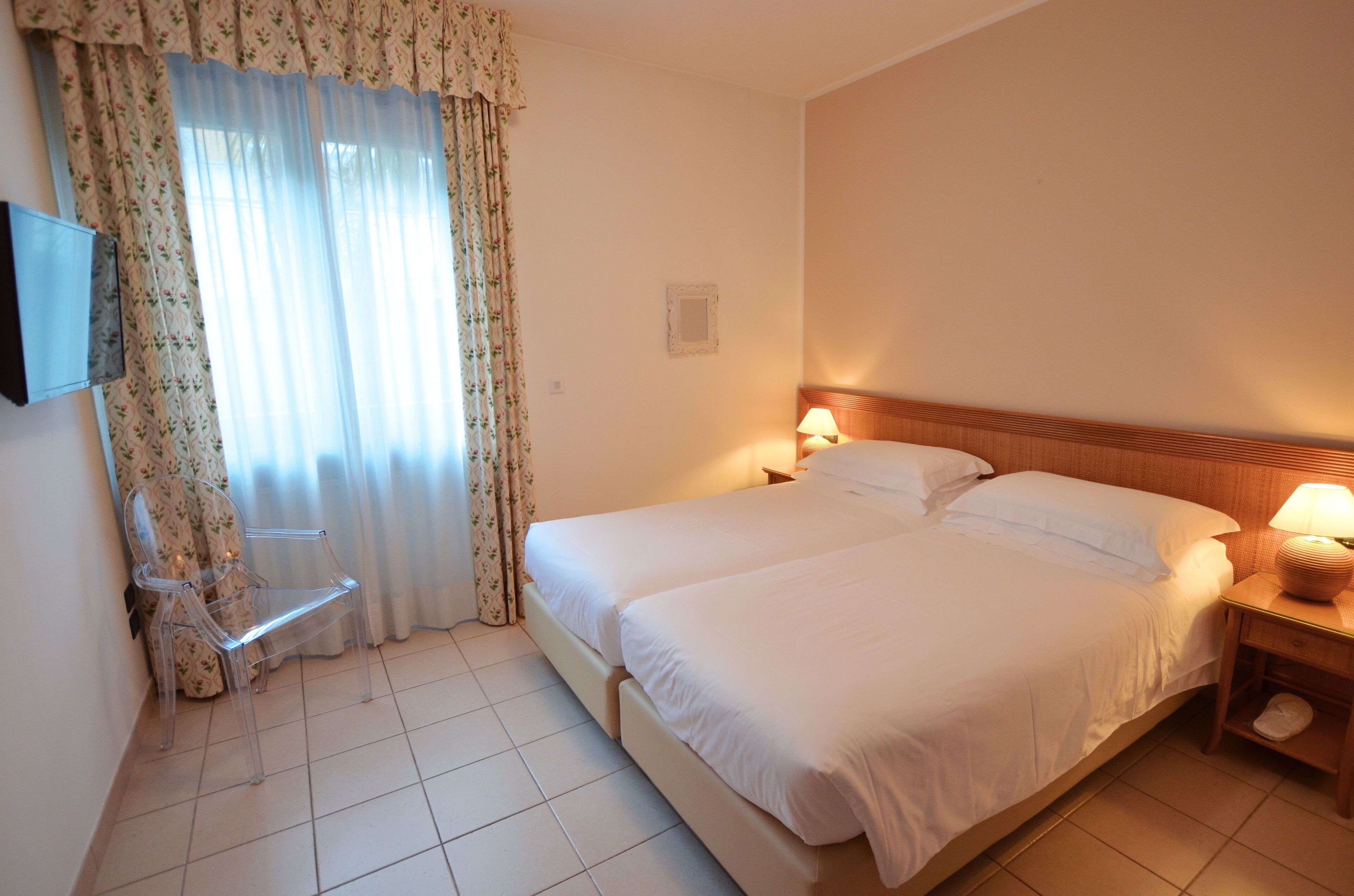 Ein Hotelzimmer mit einem großen Bett, einem Sessel, einem Nachttisch mit Lampe und einem fenster mit Vorhängen.