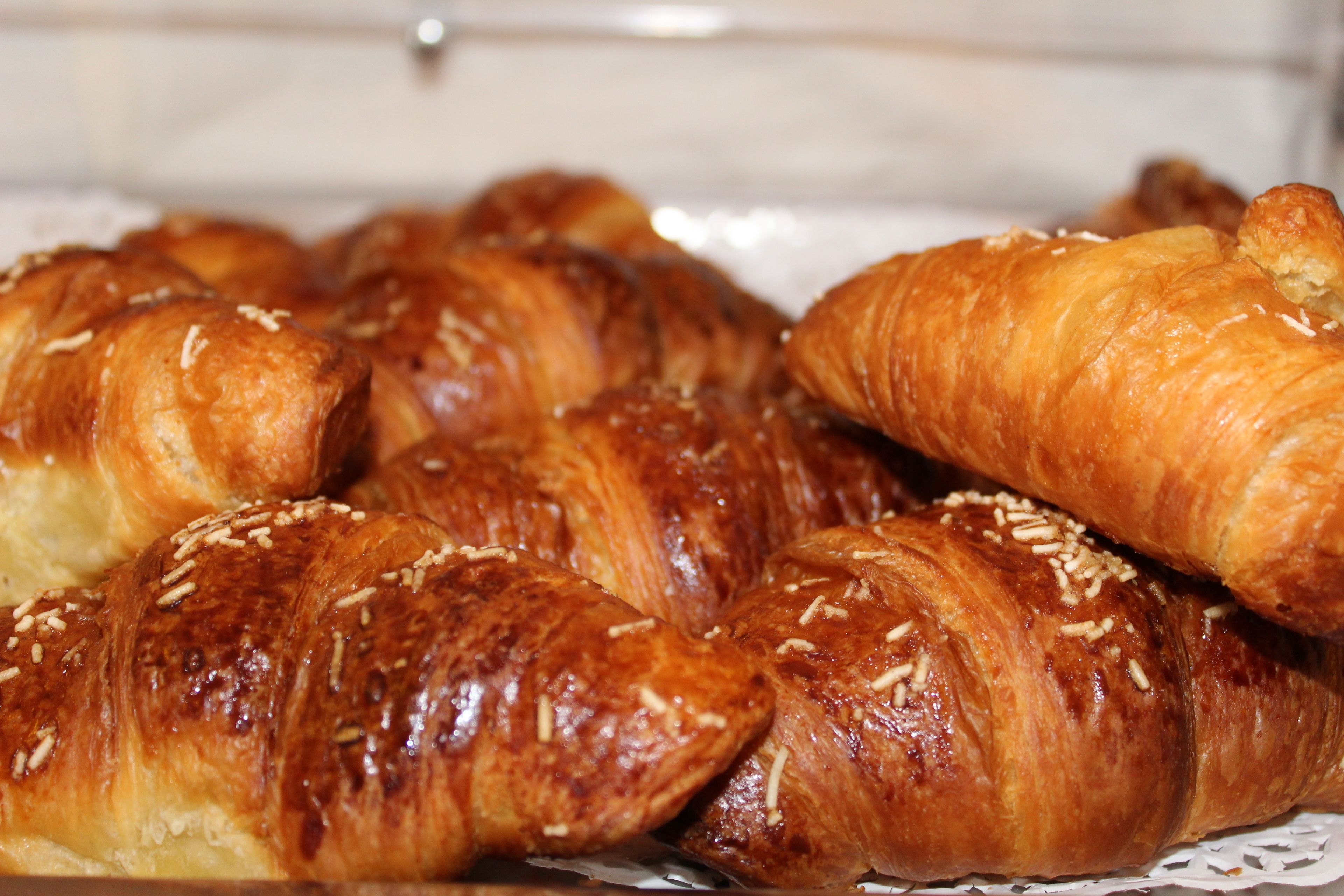 A tray of golden-brown croissants with sesame seeds, arranged on a white plate.