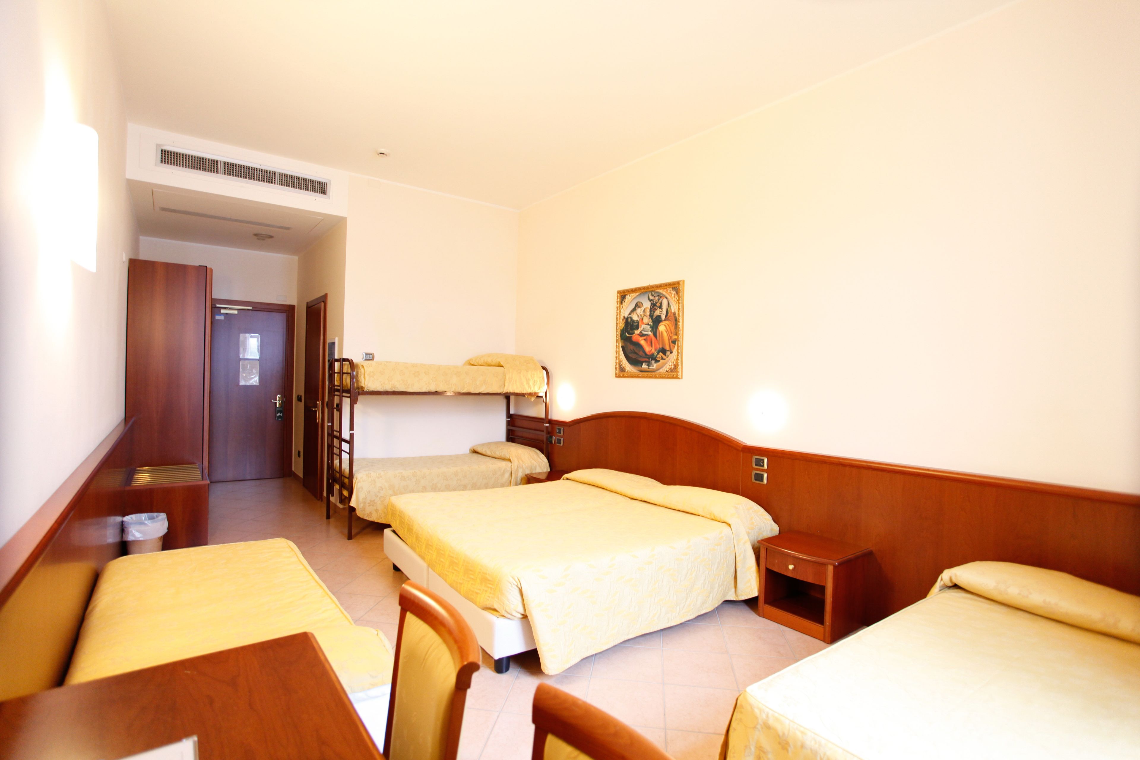 A hotel room with three beds, a wooden desk, and a small bedside table.