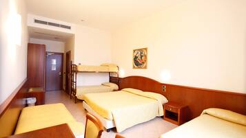 A hotel room with three beds, a wooden desk, and a small bedside table.