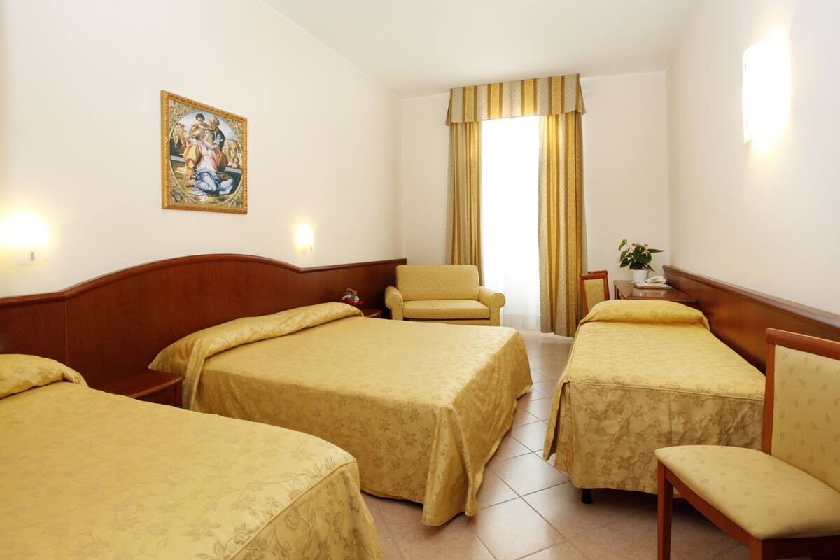 A hotel room with two beds, a chair, a small table, and a painting on the wall.