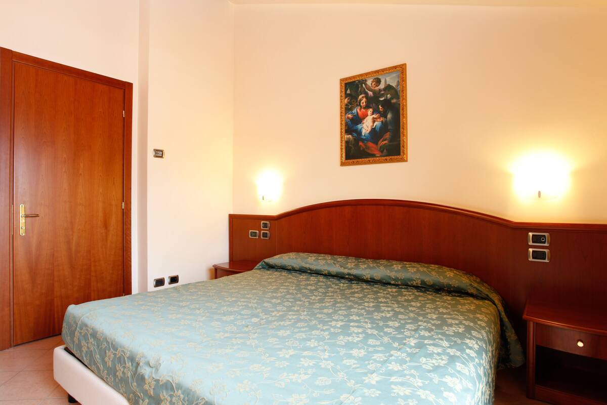 A hotel room with a wooden bed, a nightstand, a wall-mounted painting, and a door.