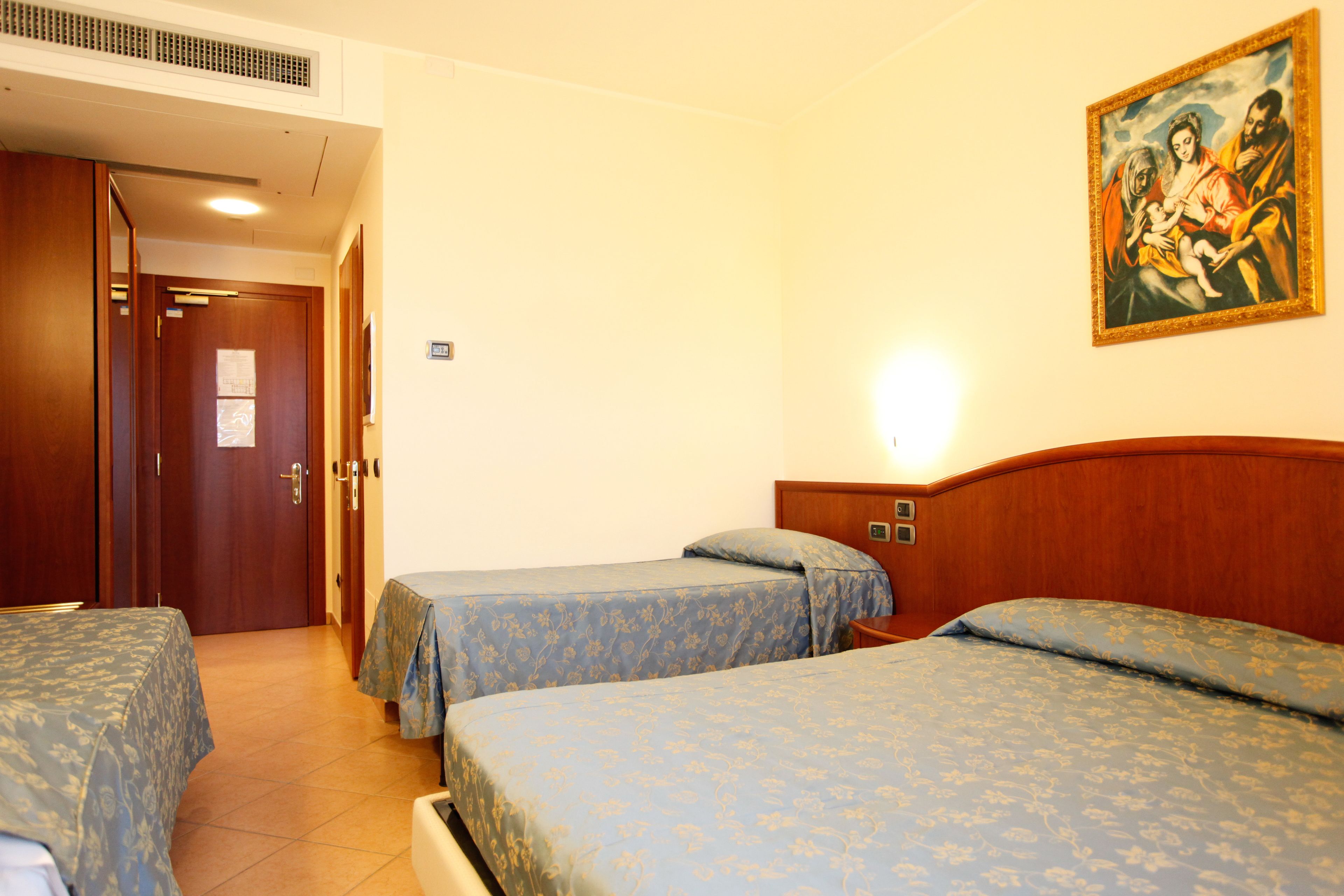 Habitación de hotel con dos camas individuales, cabecero de madera, un cuadro en la pared y una puerta que da a otra habitación.