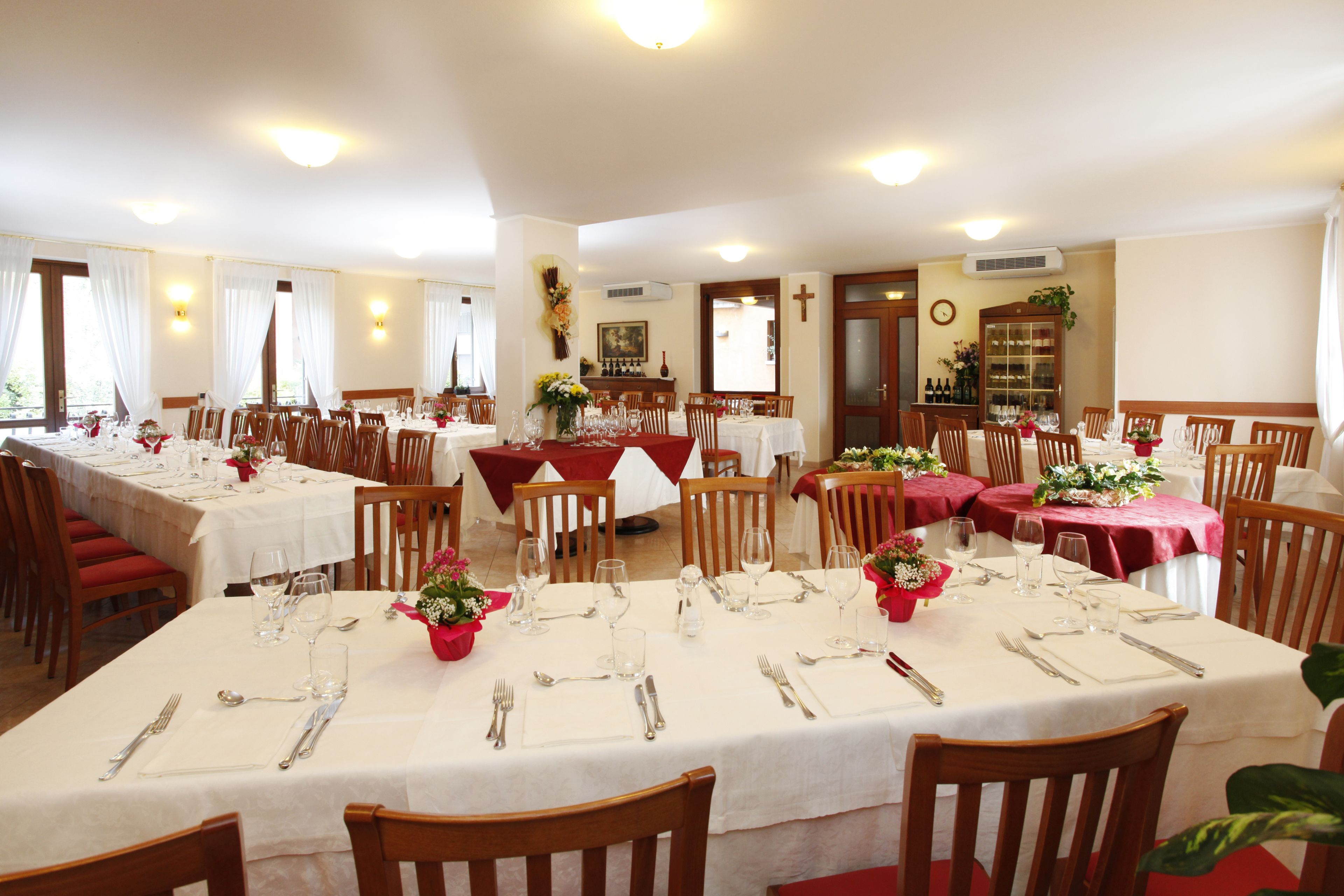 A dining area with multiple tables set for service, wooden chairs, and a cross on the wall.