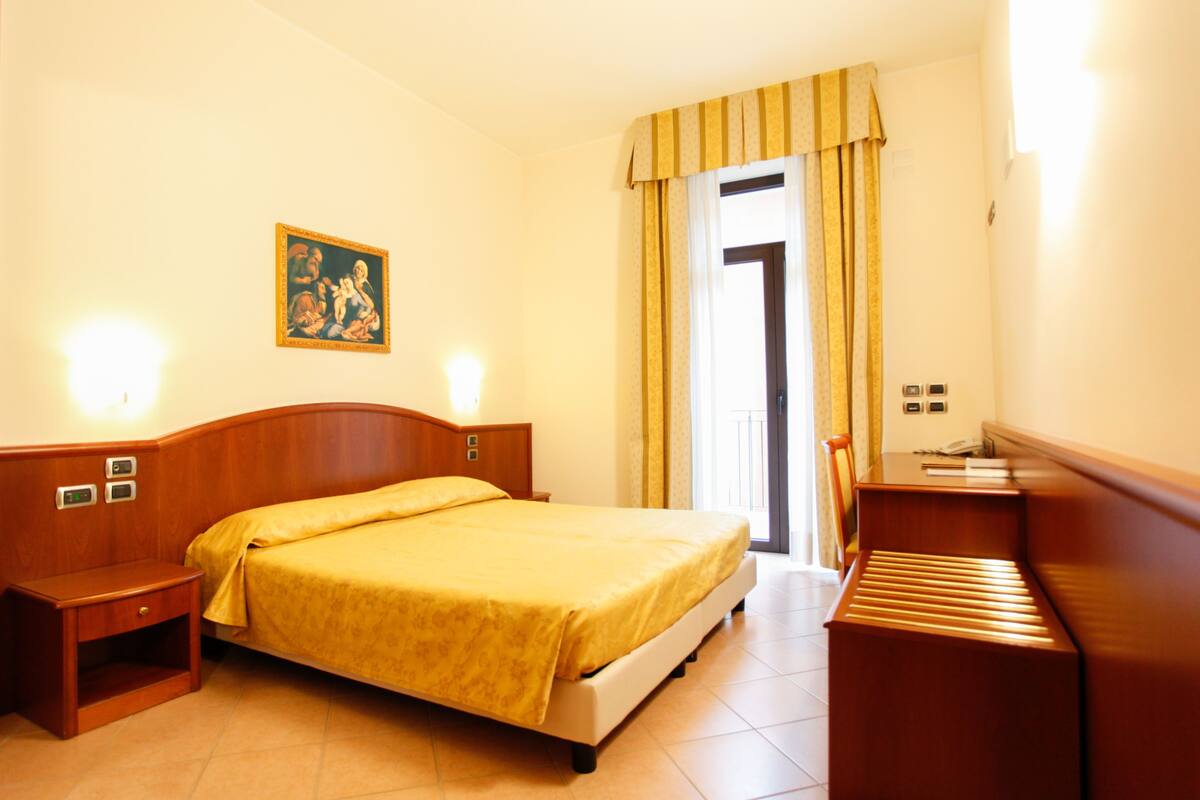 A hotel room with a bed, bedside table, lamp, and a painting on the wall.