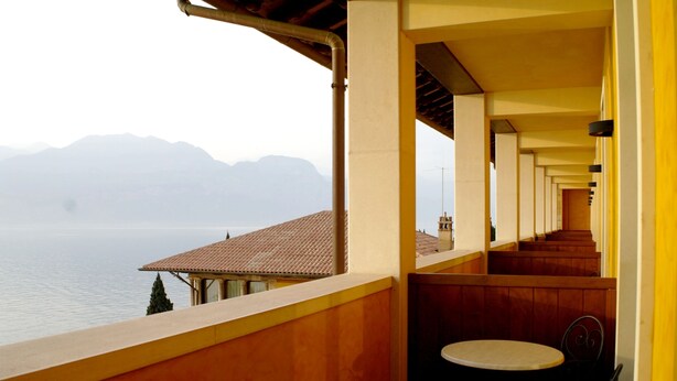 Un balcón con vistas a un lago y montañas, bancos de madera y una mesa con sillas.