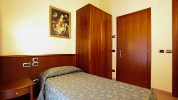 A hotel room with a bed, a wooden wardrobe, a nightstand, and a painting on the wall.
