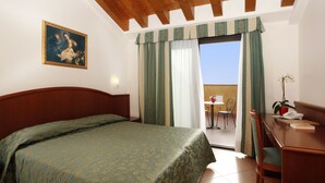Un dormitorio con cama, escritorio y silla. Se ve una ventana con cortinas y vistas al cielo.