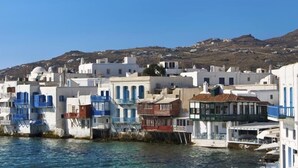 A coastal town with white buildings, some with blue accents, and a clear view of the sea.