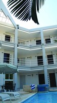 Un edificio de varios pisos con balcones, piscina y mobiliario exterior.