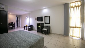Quarto de hotel com cama, escrivaninha, cadeira, televisão e janela com cortinas.