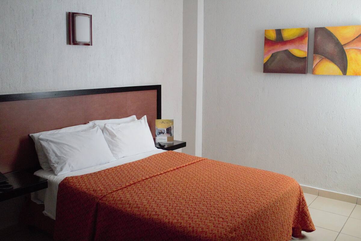 A hotel room with a bed, a nightstand, and two paintings on the wall.
