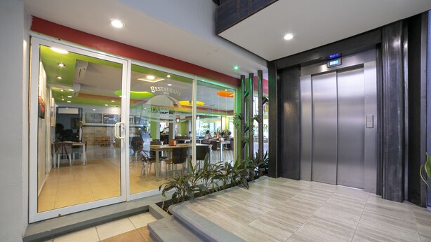 Um edifício moderno com um restaurante visível através de portas de vidro, um elevador e uma escadaria que leva a uma entrada.