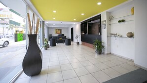 Um saguão de hotel com teto amarelo, balcão de recepção, área de estar e um vaso grande.
