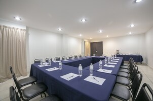 Un salón de conferencias con una larga mesa, sillas, botellas de agua y tarjetas de identificación.