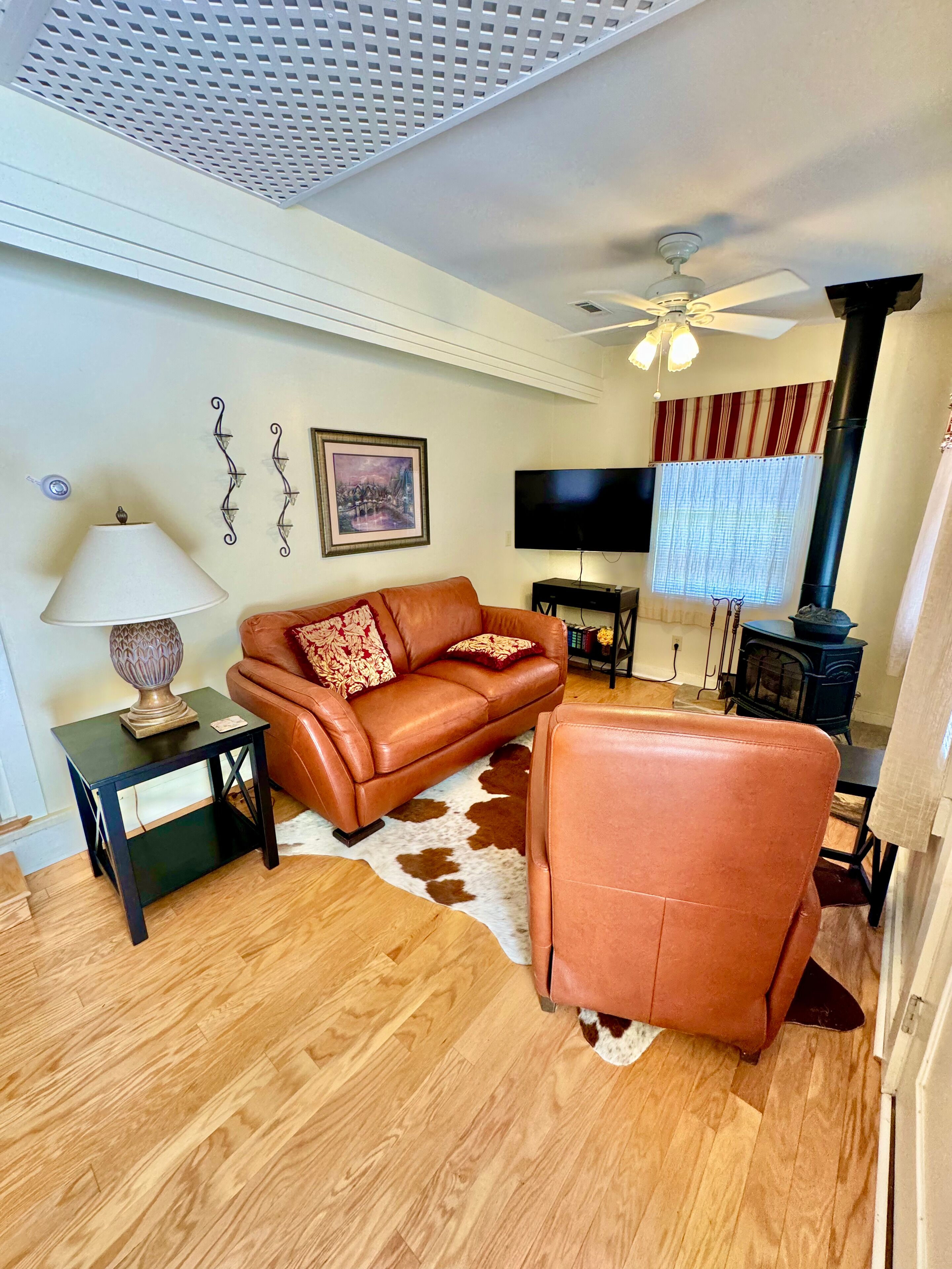 A living room with a sofa, a chair, a TV, a lamp, a fireplace, and a ceiling fan.