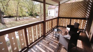 A wooden deck with a table and chairs, overlooking a yard with trees and a house. - Riverbend Motel & Cabins (Helen)