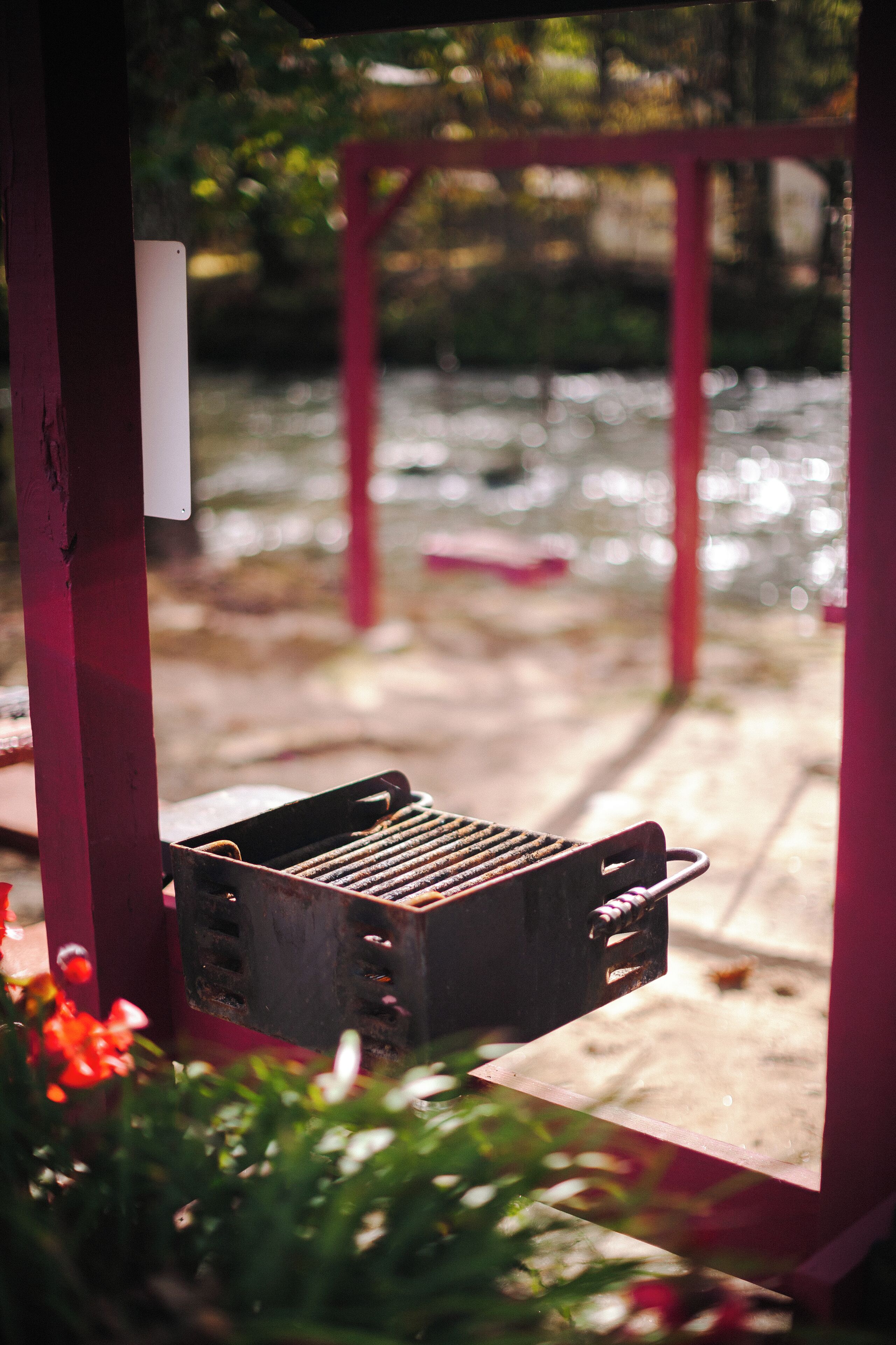 A grill outdoors with a wooden deck and a pink structure in the background.