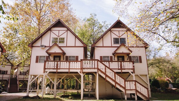Two wooden cabins with balconies and stairs, surrounded by trees. - Riverbend Motel & Cabins (Helen)