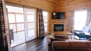 A cozy cabin interior with a fireplace, wooden walls, a sofa, and a television. - Riverbend Motel & Cabins (Helen)