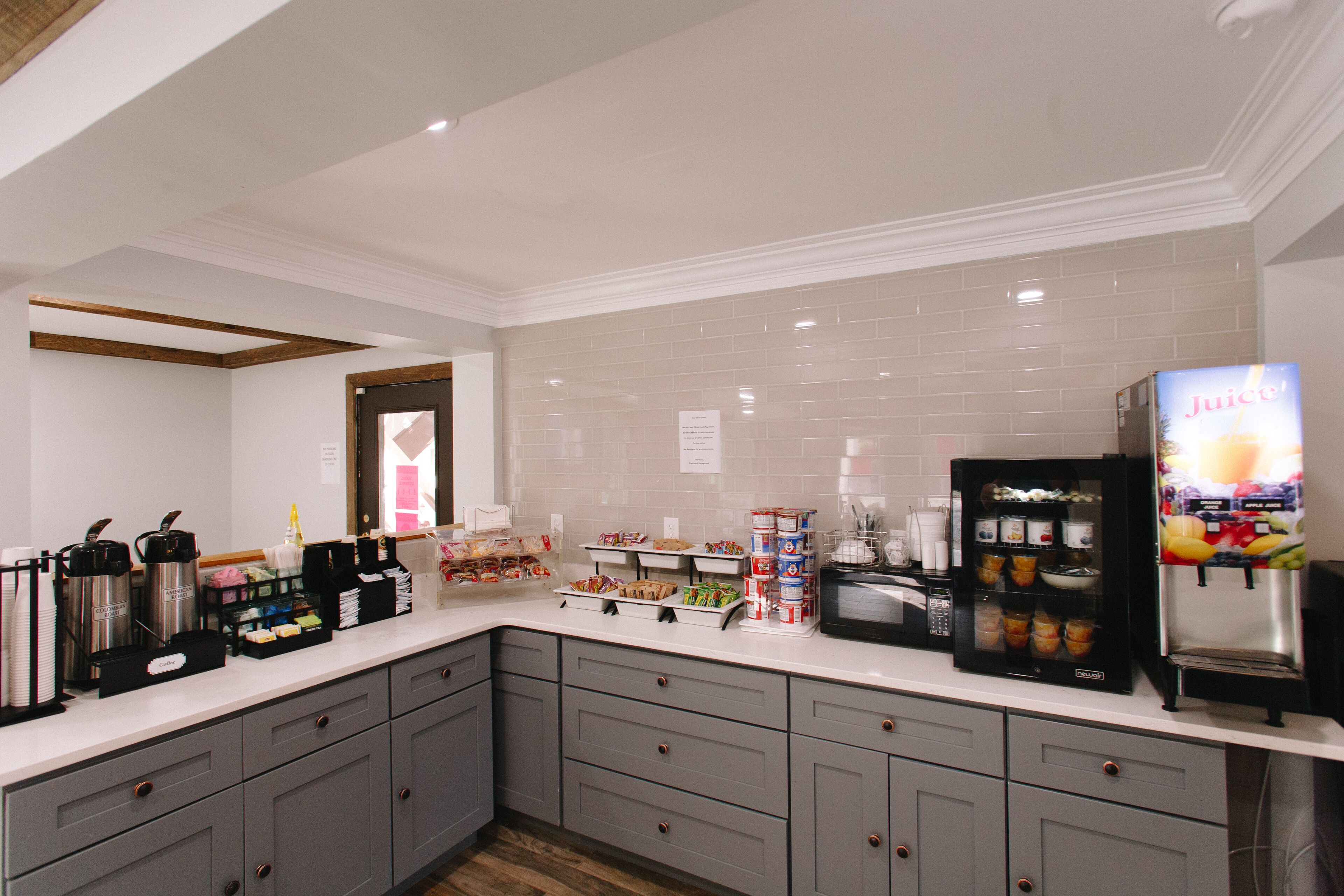 A modern kitchen with a white countertop, grey cabinets, a juice dispenser, and a coffee machine.