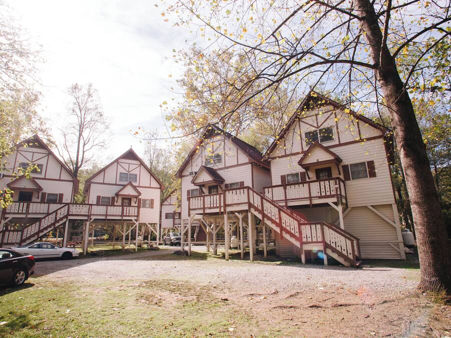 A row of wooden cabins with external staircases, a gravel driveway, and a tree in the foreground.