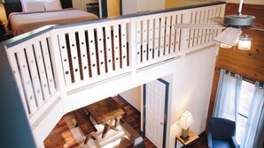 A multi-level room with a wooden floor, a bed on the upper level, a desk, and a chair. - Riverbend Motel & Cabins (Helen)