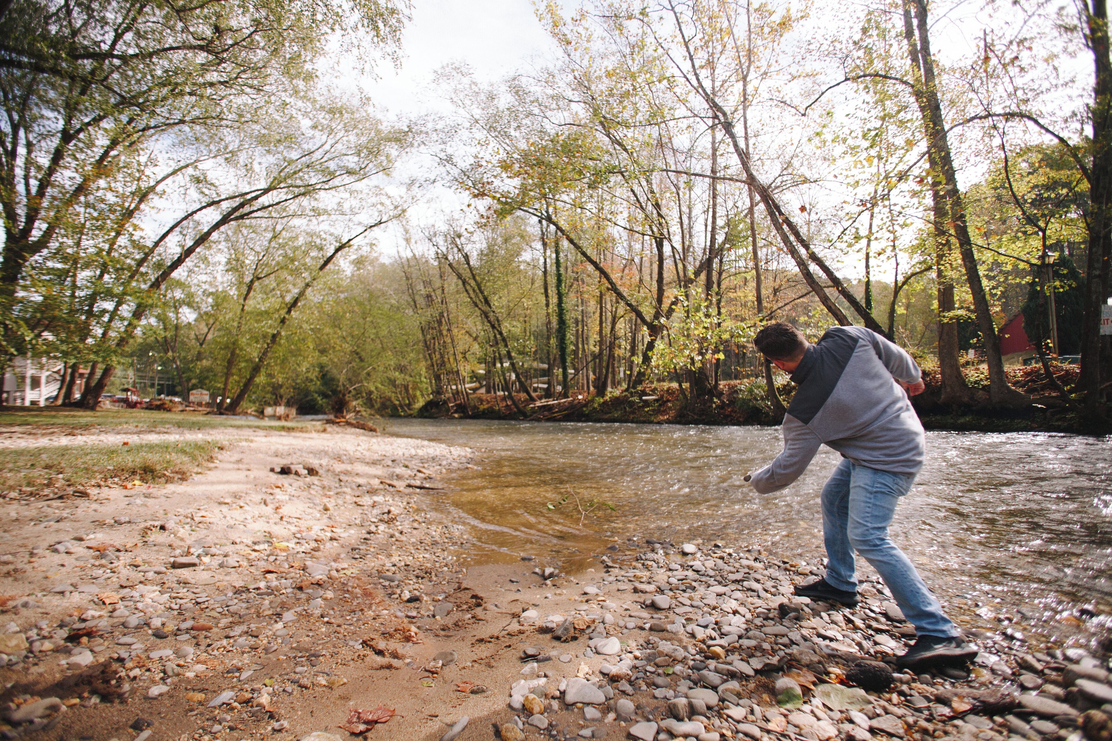 A person standing by a river with trees in the background.